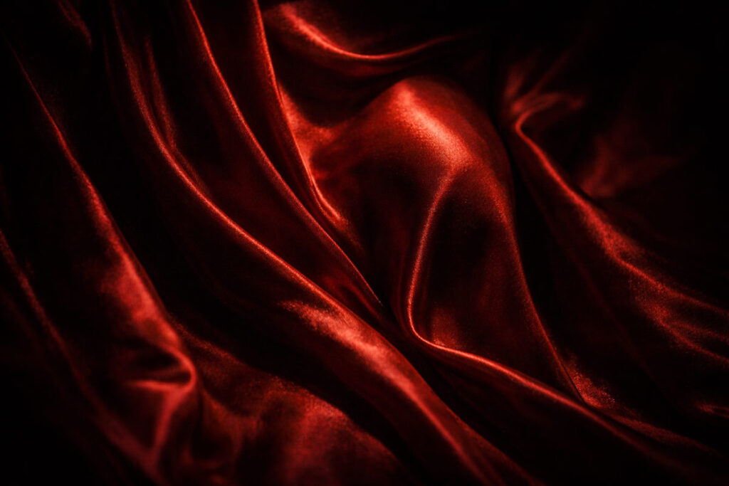 Fotografía artística y tenebrista de pliegues de terciopelo rojo iluminados como un altar sagrado, metáfora visual para el poema erótico "Un coño que diga Amén".
