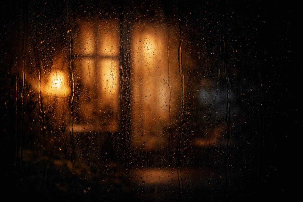 Fotografía artística de lluvia en una ventana con luces cálidas, inspirada en el final del relato El sexo de los ángeles de Mario Benedetti.
